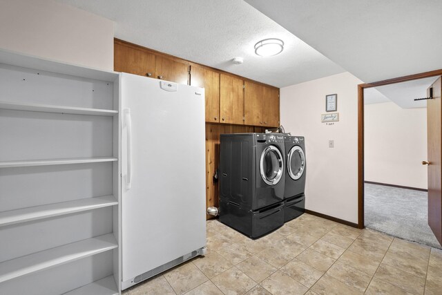 clothes washing area with a textured ceiling, washing machine and dryer, light carpet, baseboards, and cabinet space