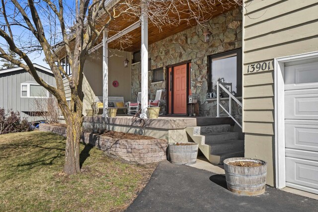 doorway to property with covered porch, stone siding, and a garage