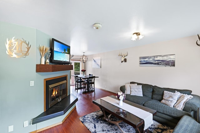 living area featuring a glass covered fireplace, a notable chandelier, baseboards, and wood finished floors