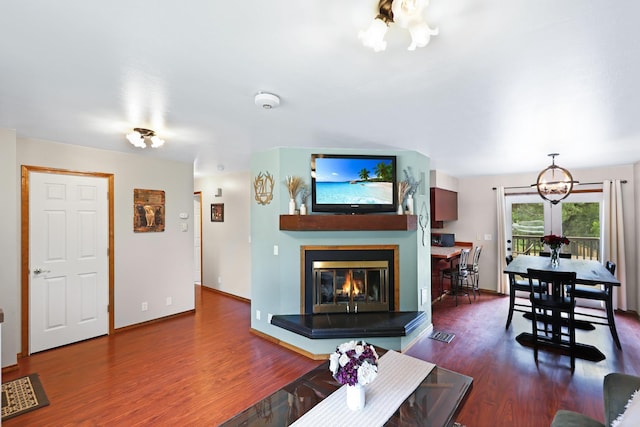 living room featuring an inviting chandelier, baseboards, a multi sided fireplace, and wood finished floors