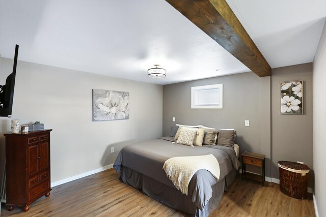 bedroom with light wood-style floors, baseboards, and beam ceiling