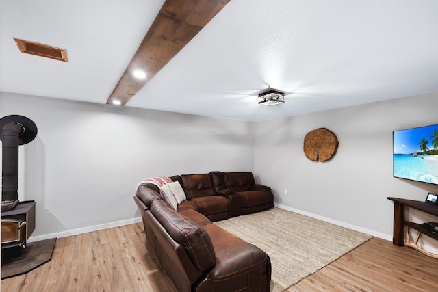 living room with visible vents, a wood stove, wood finished floors, beamed ceiling, and baseboards