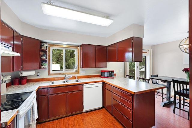 kitchen featuring white appliances, wood finished floors, a peninsula, under cabinet range hood, and a sink