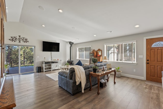 living area featuring baseboards, vaulted ceiling, recessed lighting, a wood stove, and wood finished floors