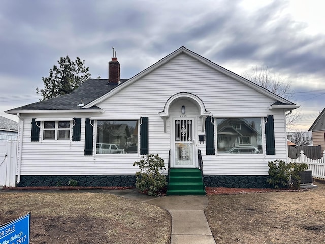 bungalow-style house featuring cooling unit, a chimney, roof with shingles, and fence