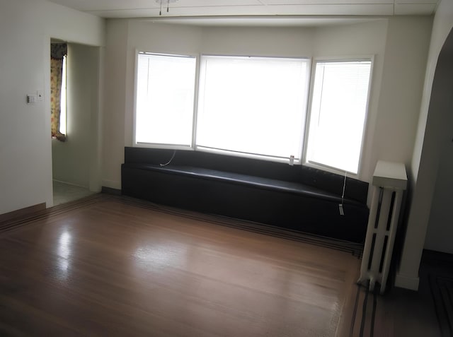 unfurnished living room featuring baseboards, wood finished floors, and radiator heating unit