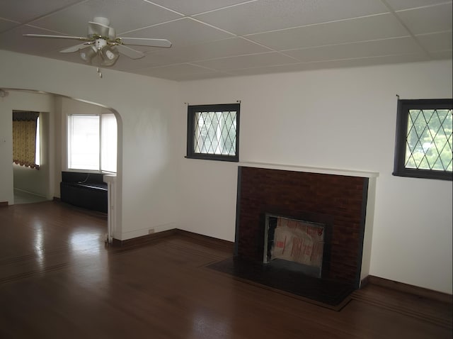 unfurnished living room with arched walkways, a fireplace, baseboards, and wood finished floors