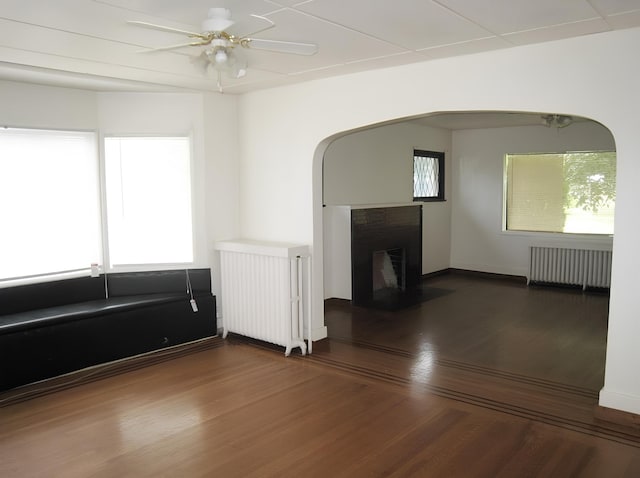 unfurnished living room with radiator, wood finished floors, radiator heating unit, and a brick fireplace