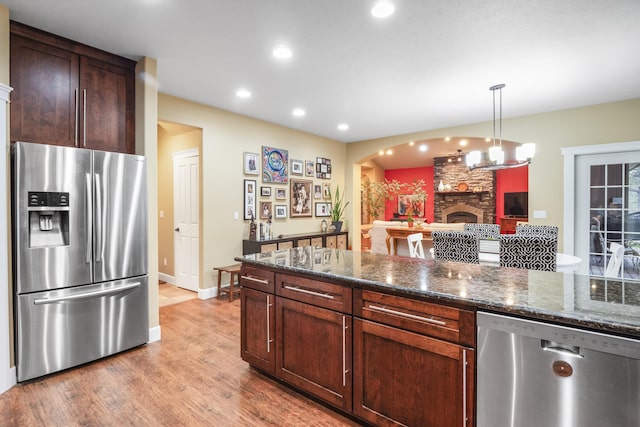 kitchen featuring appliances with stainless steel finishes, a fireplace, dark stone counters, and wood finished floors