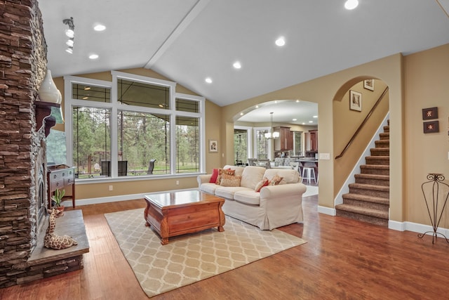 living area with wood finished floors, arched walkways, baseboards, stairs, and vaulted ceiling