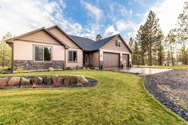 view of front of house featuring a garage, stone siding, a front lawn, and driveway