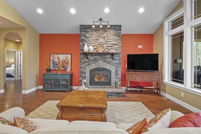 living room featuring arched walkways, a fireplace, baseboards, and wood finished floors