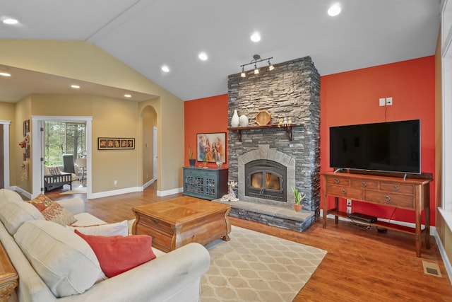 living area featuring wood finished floors, visible vents, arched walkways, a stone fireplace, and vaulted ceiling