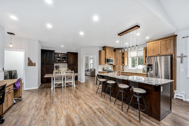 kitchen featuring light wood-type flooring, independent washer and dryer, a center island with sink, a kitchen breakfast bar, and appliances with stainless steel finishes