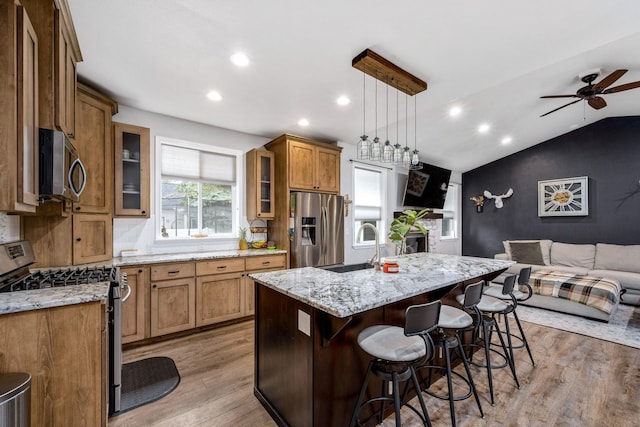 kitchen with brown cabinetry, light wood-style flooring, a sink, stainless steel appliances, and open floor plan