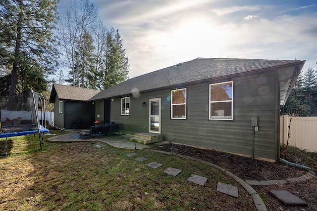 rear view of house with a patio area, a lawn, a trampoline, and fence