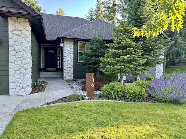 view of front of home featuring stone siding, a front lawn, and roof with shingles