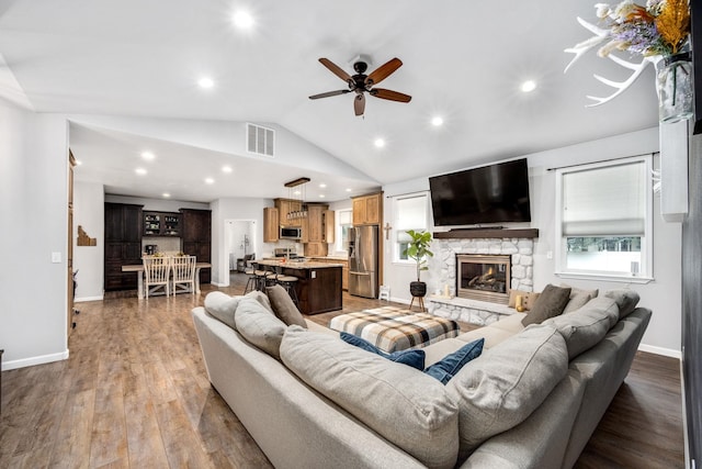 living room with wood finished floors, visible vents, baseboards, a stone fireplace, and vaulted ceiling