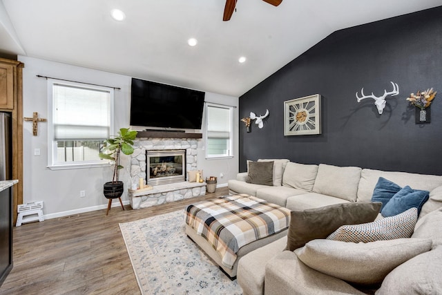 living area featuring an accent wall, baseboards, lofted ceiling, a stone fireplace, and wood finished floors