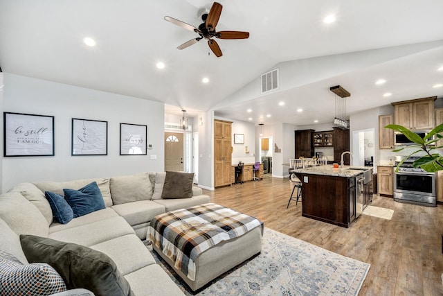 living area with visible vents, light wood-style floors, ceiling fan, and vaulted ceiling