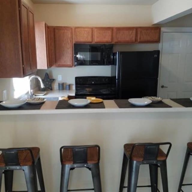 kitchen with a kitchen breakfast bar, black appliances, and light countertops