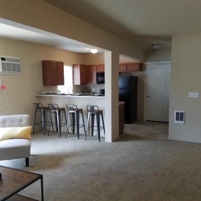 kitchen with a wall mounted air conditioner, black appliances, a kitchen breakfast bar, brown cabinetry, and carpet flooring