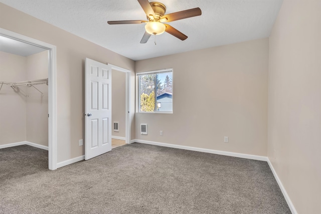 unfurnished bedroom featuring a walk in closet, carpet flooring, baseboards, and visible vents