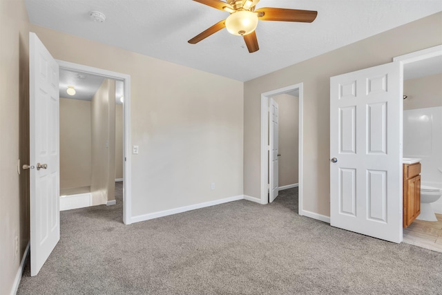 unfurnished bedroom featuring a ceiling fan, baseboards, ensuite bathroom, and light carpet