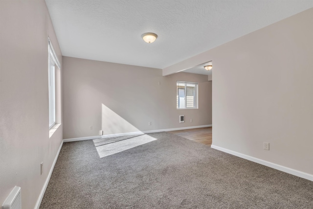 spare room featuring visible vents, carpet floors, a textured ceiling, and baseboards