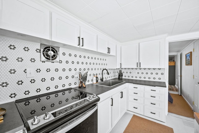 kitchen with a sink, decorative backsplash, stainless steel range with electric cooktop, white cabinetry, and dark countertops