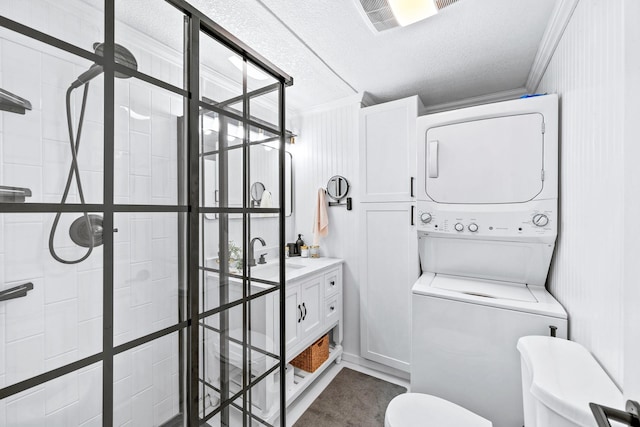 full bath featuring toilet, ornamental molding, stacked washer and dryer, tiled shower, and a textured ceiling