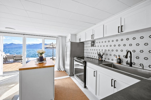 kitchen with stainless steel electric stove, butcher block countertops, a sink, white cabinetry, and tasteful backsplash