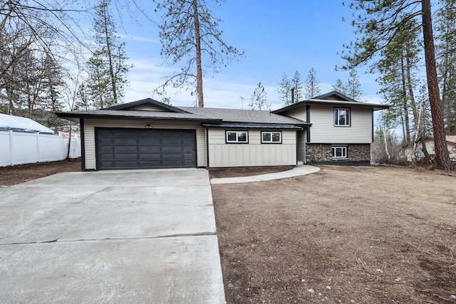 tri-level home with board and batten siding, fence, concrete driveway, stone siding, and an attached garage