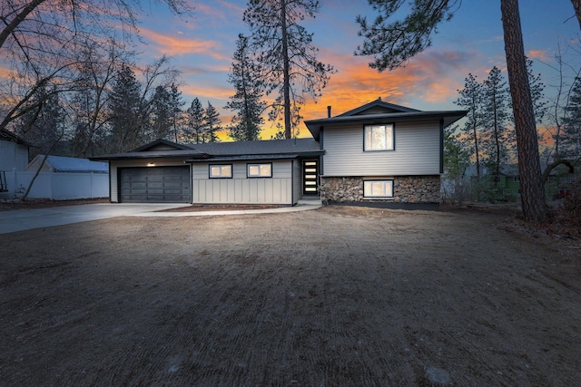 split level home featuring stone siding, concrete driveway, and a garage