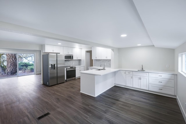 kitchen with dark wood finished floors, white cabinetry, appliances with stainless steel finishes, a peninsula, and light countertops