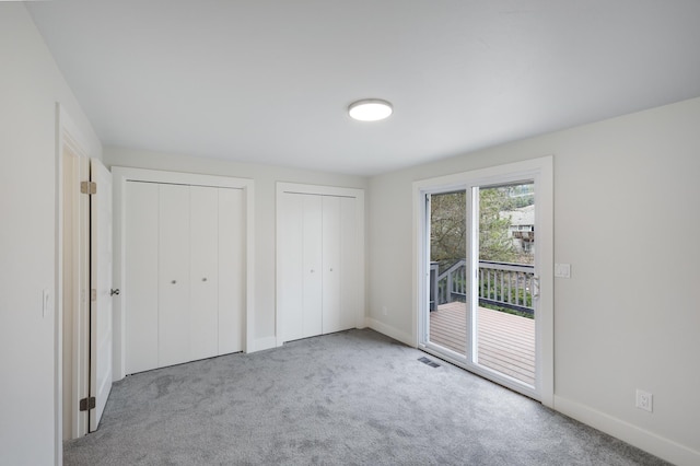 unfurnished bedroom with baseboards, visible vents, carpet floors, multiple closets, and access to outside