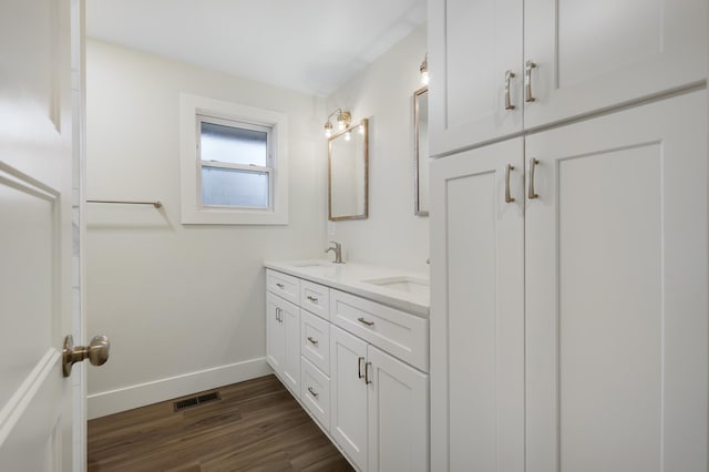 bathroom with wood finished floors, baseboards, visible vents, double vanity, and a sink