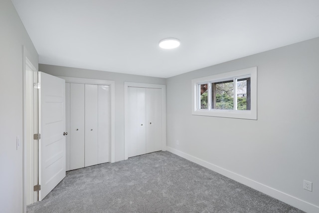 unfurnished bedroom with baseboards, carpet, and multiple closets