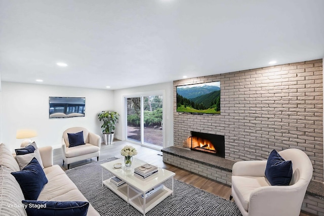 living area featuring wood finished floors, recessed lighting, a fireplace, and brick wall