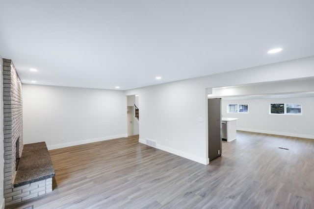 below grade area with stairway, a brick fireplace, baseboards, and light wood-type flooring