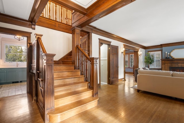 staircase with beam ceiling, ornamental molding, and wood finished floors