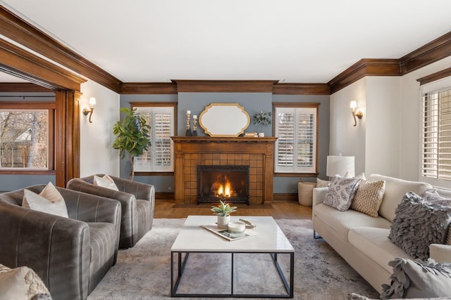 living area featuring a tile fireplace, crown molding, baseboards, and wood finished floors