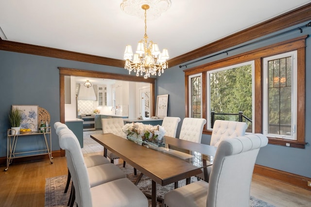 dining space featuring a notable chandelier, light wood-style flooring, crown molding, and baseboards