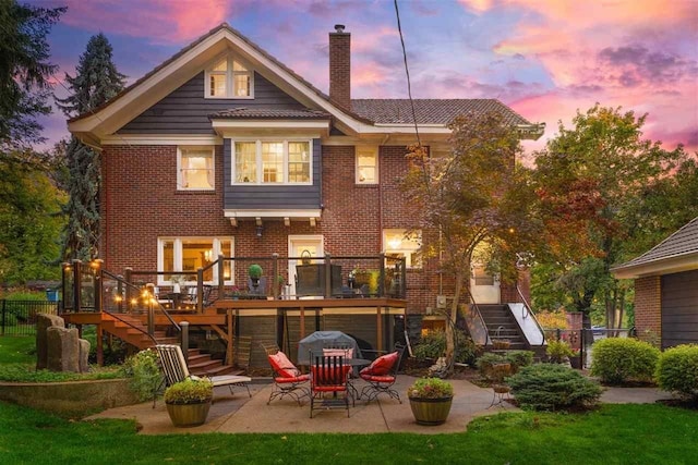 back of property at dusk featuring a patio, stairs, fence, brick siding, and a chimney