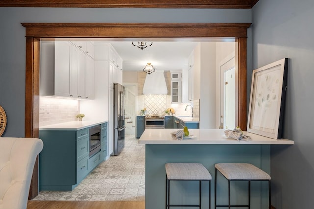 kitchen featuring a peninsula, custom range hood, blue cabinets, white cabinetry, and high quality appliances