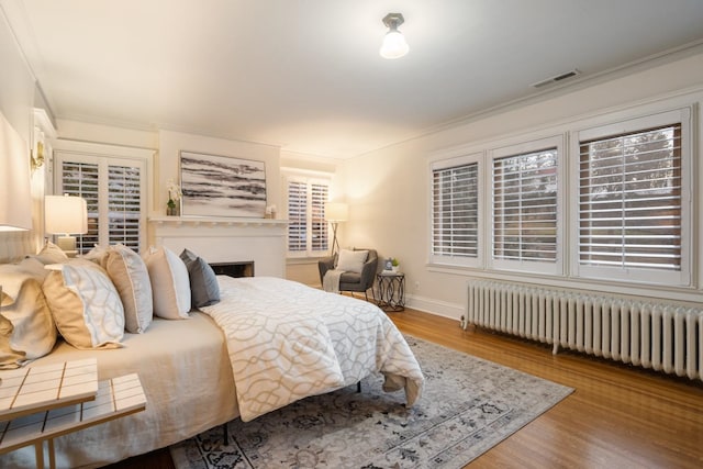 bedroom with visible vents, ornamental molding, radiator, and wood finished floors