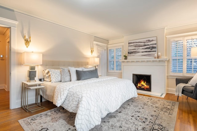 bedroom featuring baseboards, a lit fireplace, and wood finished floors