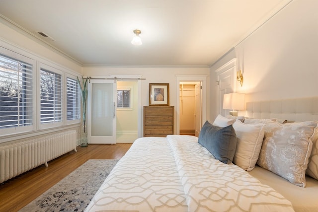 bedroom with wood finished floors, visible vents, radiator heating unit, a barn door, and crown molding