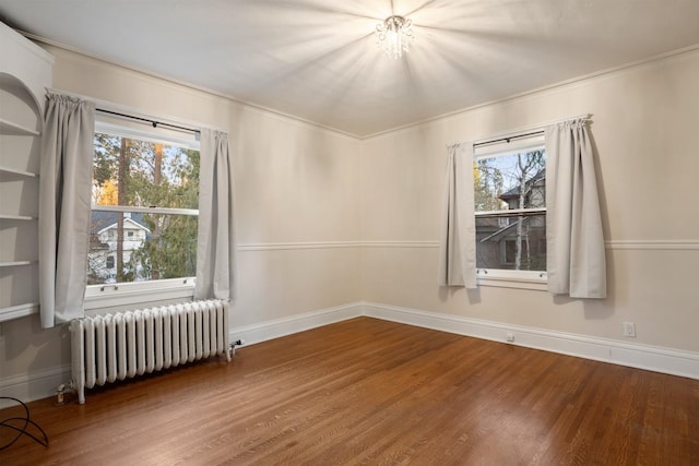 spare room featuring baseboards, wood finished floors, and radiator heating unit