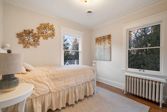 bedroom featuring crown molding, radiator, wood finished floors, and visible vents